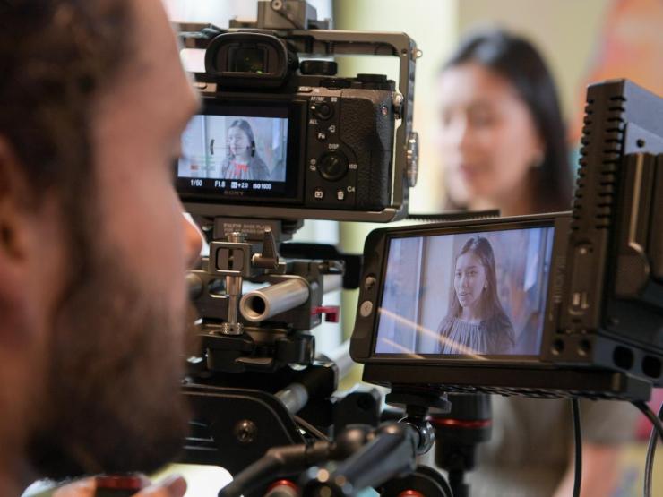 A student looking into a video camera, with another student in the background