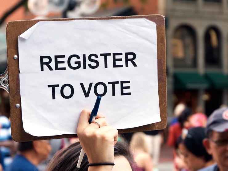 Hand holding up sign reading Register to Vote