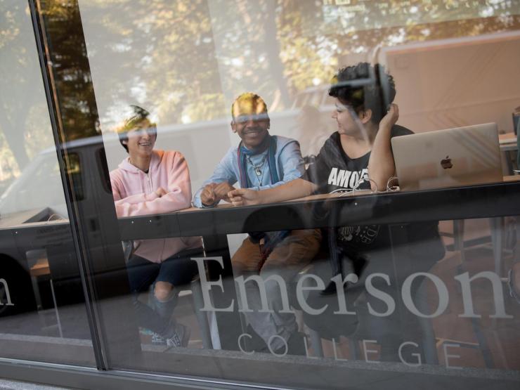 Three students sitting together at a counter behind the window of the dining center