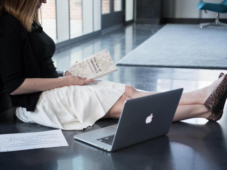 Person sitting on floor with book and laptop