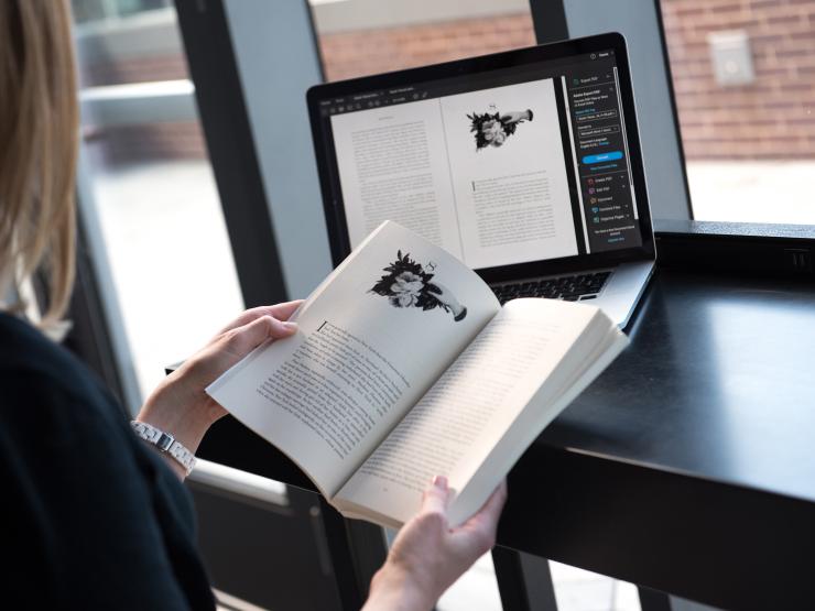 Person with book and viewing the same book layout on a laptop screen