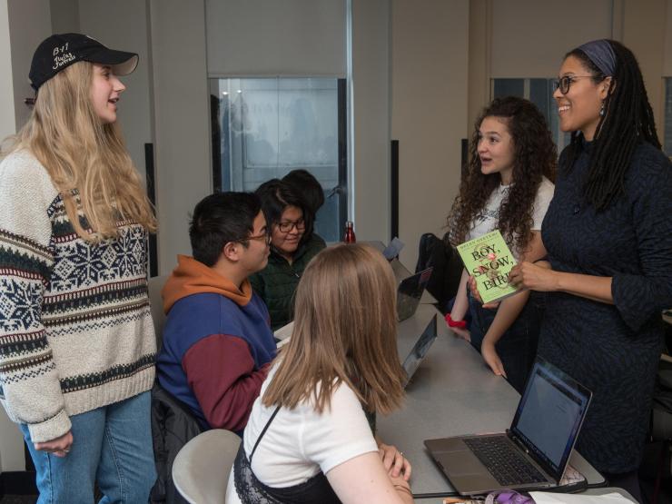 Students and teacher standing around table, some students are sitting