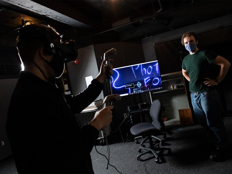 A student experiences virtual reality in a dark room while another person watches