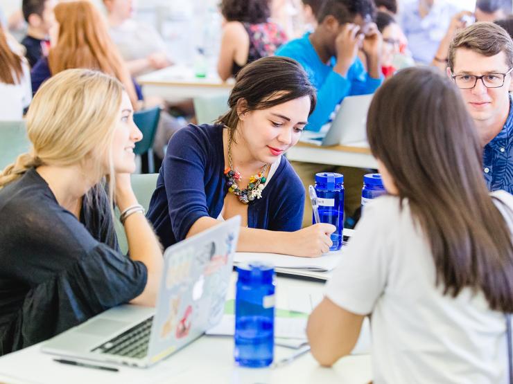 Students sitting around a table in discussion with laptops and notebooks