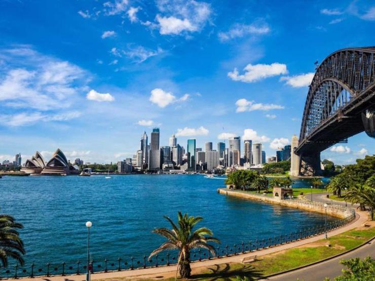 A photograph of Sydney showing the ocean, bridge, Opera House, and buildings