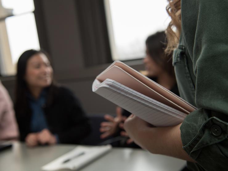 student holding notebook in foreground, student smiling in background