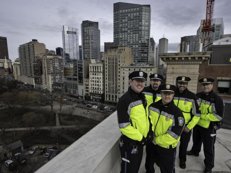 A group of Emerson College police offers standing on a rooftop overlooking Boston Common. They are smiling at the camera.