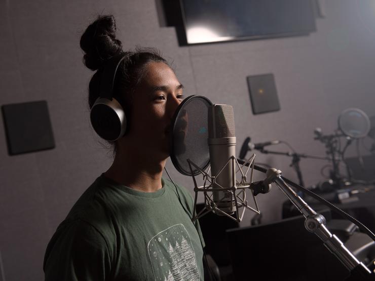 Student in a sound room wearing headphones and speaking into a microphone