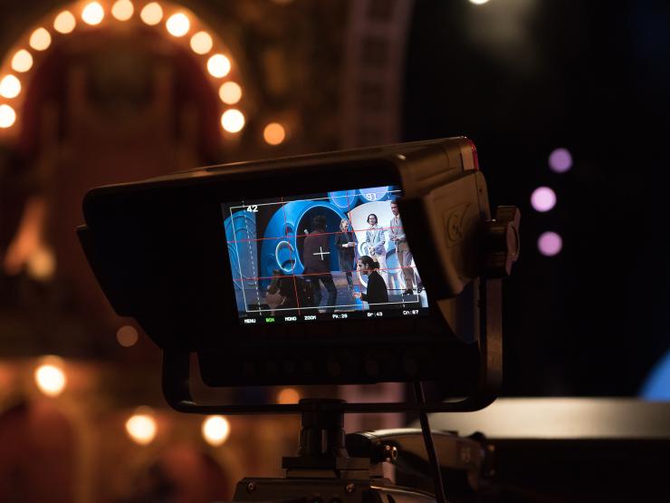 Video Monitor showing stage performance being filmed with bright lights in the back