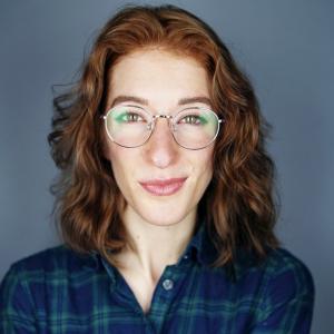 Photo of Joy facing the camera in a plaid shirt, wearing glasses