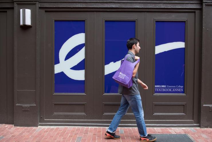 Student walking past a wall made up of panels that comprise the white Emerson "E" flourish on a dark indigo background