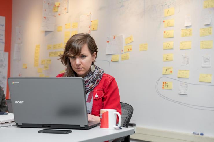 A student working at her laptop. A wall behind her is covered with sticky notes.