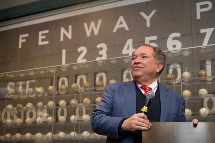 Charles stands by podium with microphone and a sign behind him